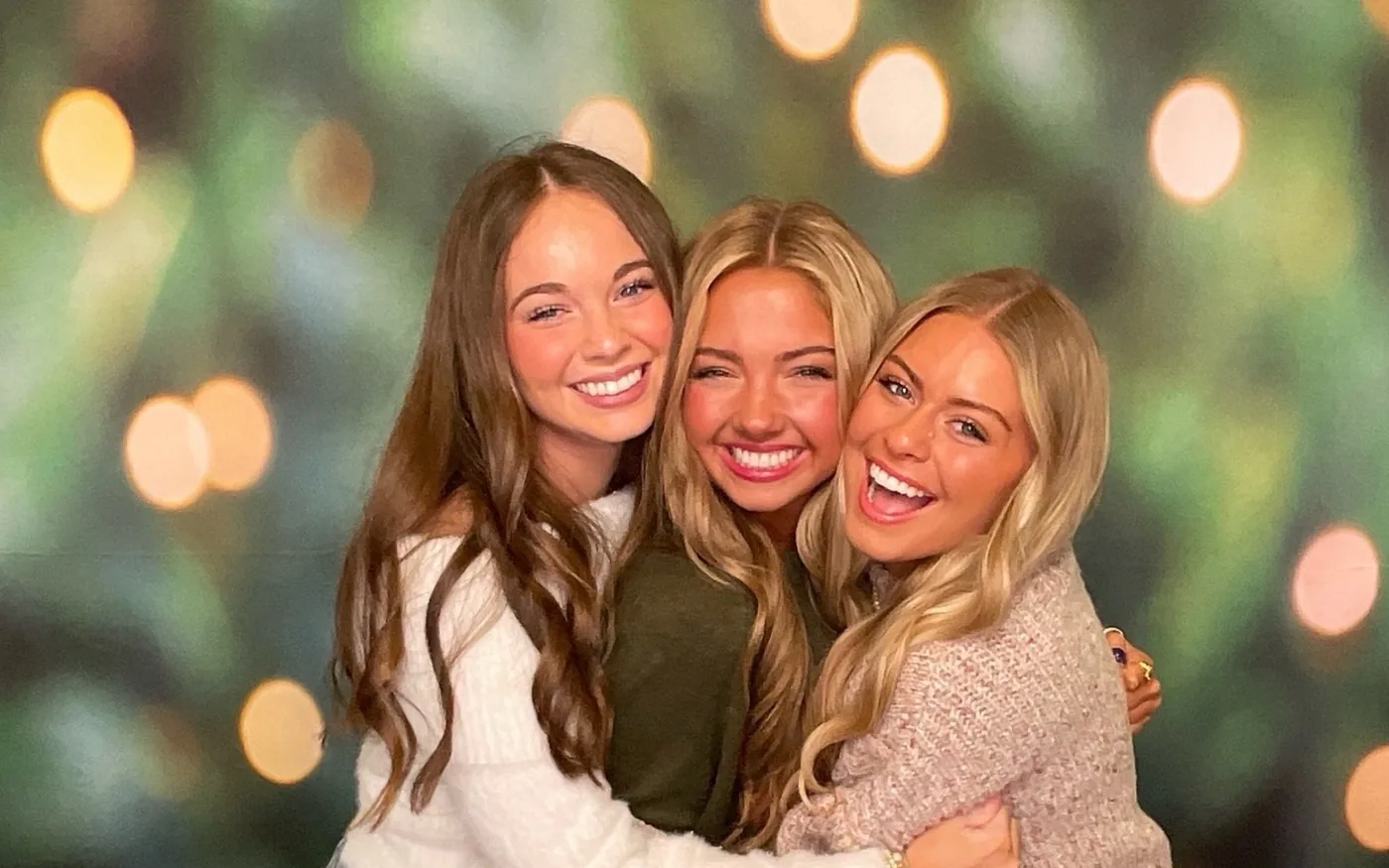 Three guests laughing together in front of a green holiday backdrop at a company Christmas party