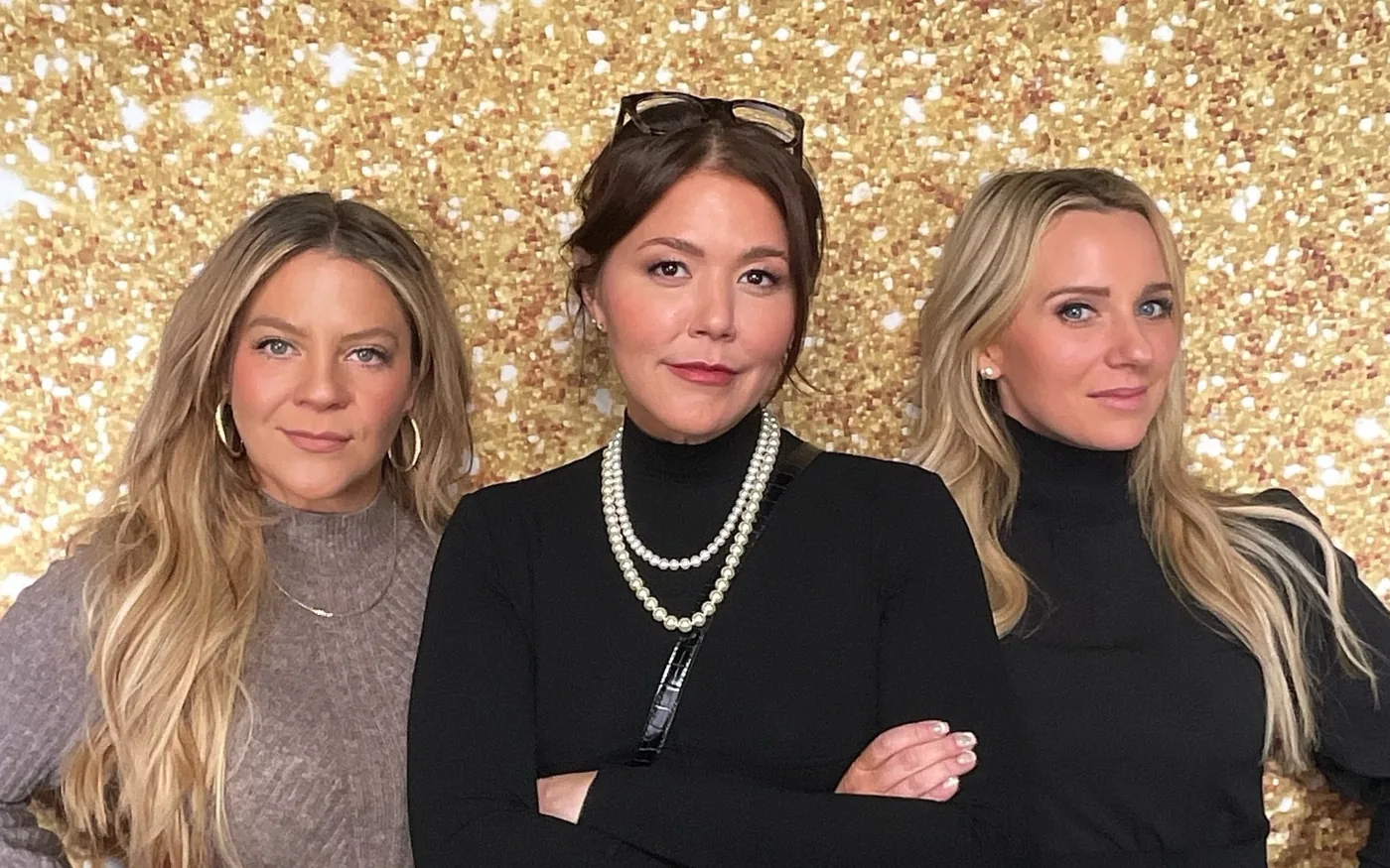 Three guests in evening wear posing in front of a gold sequin backdrop at a charity fundraiser