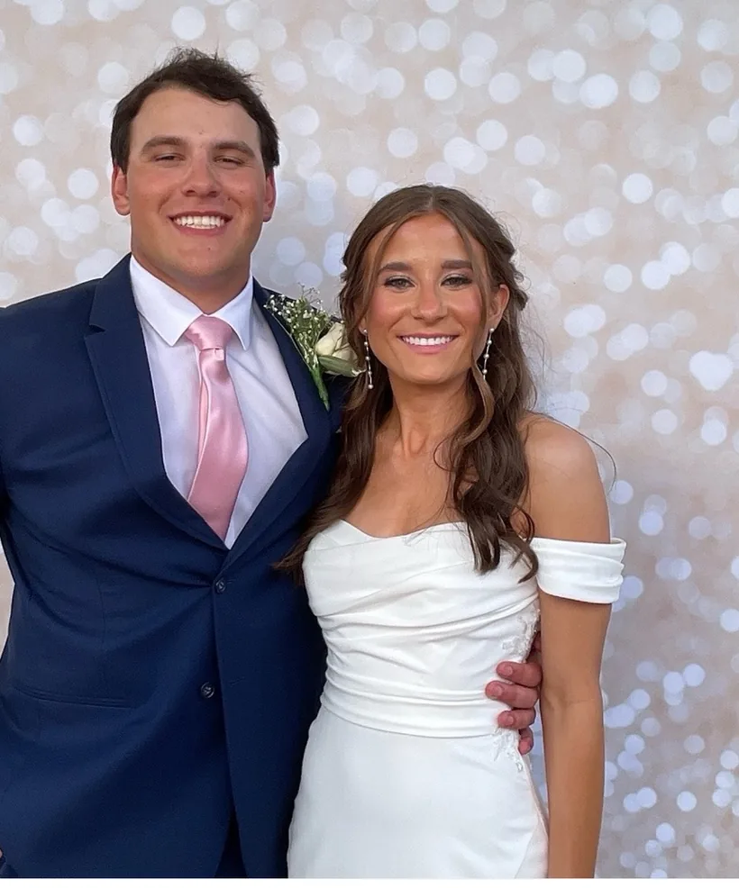 A couple in a white gown and navy suit posing in front of a soft silver backdrop