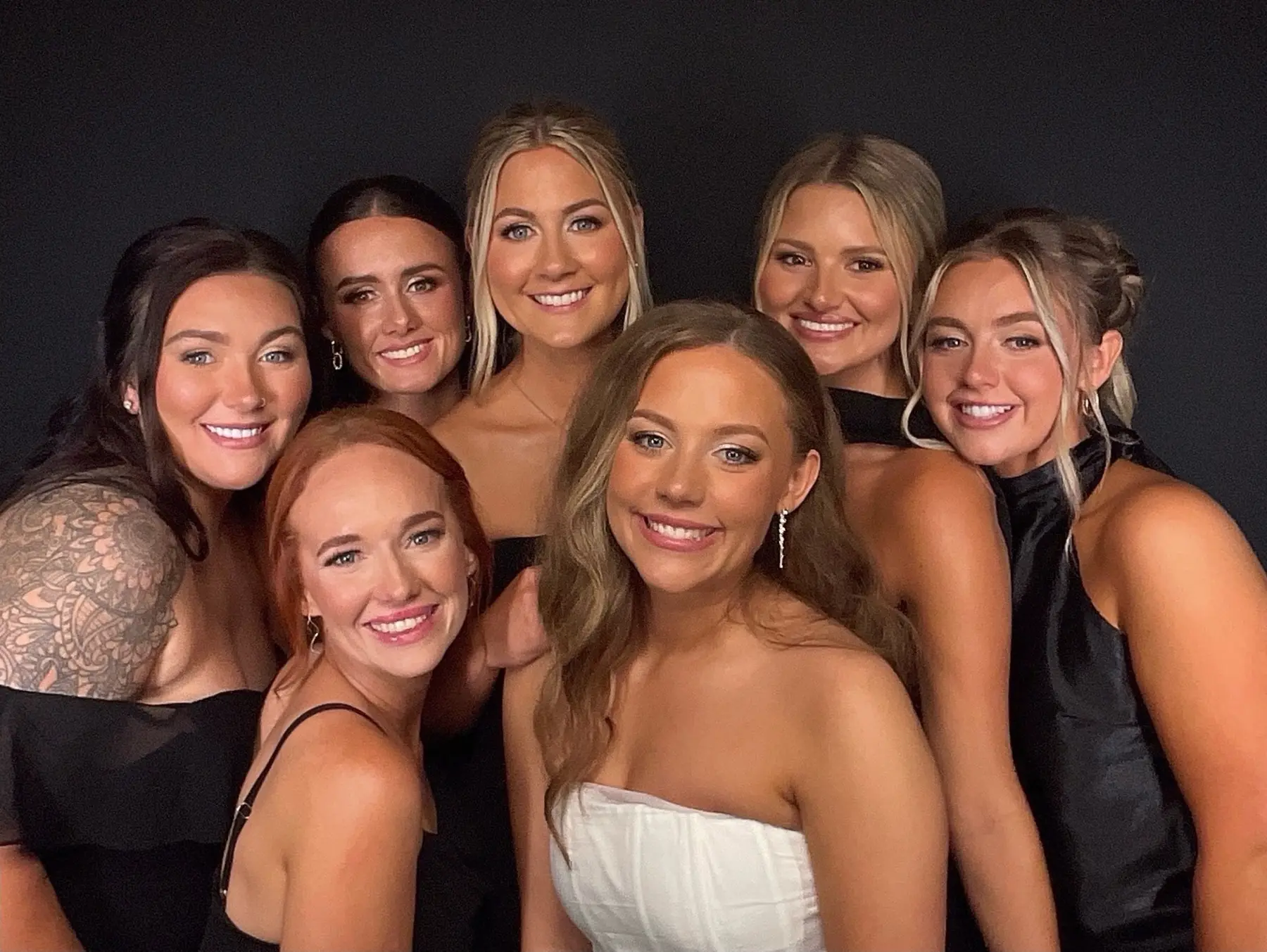 A bride and her wedding party crowded into the Candid Creative open air photo booth against a black backdrop
