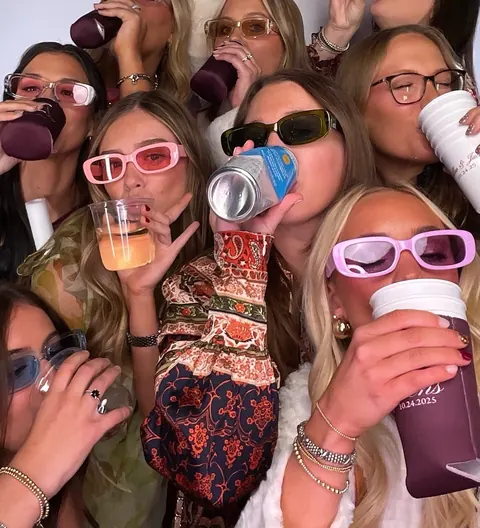 A group of guests crowded into the photo booth with drinks and colorful sunglasses