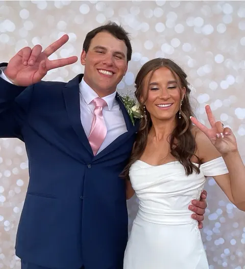 A bride and groom throwing peace signs in the booth against a soft silver backdrop