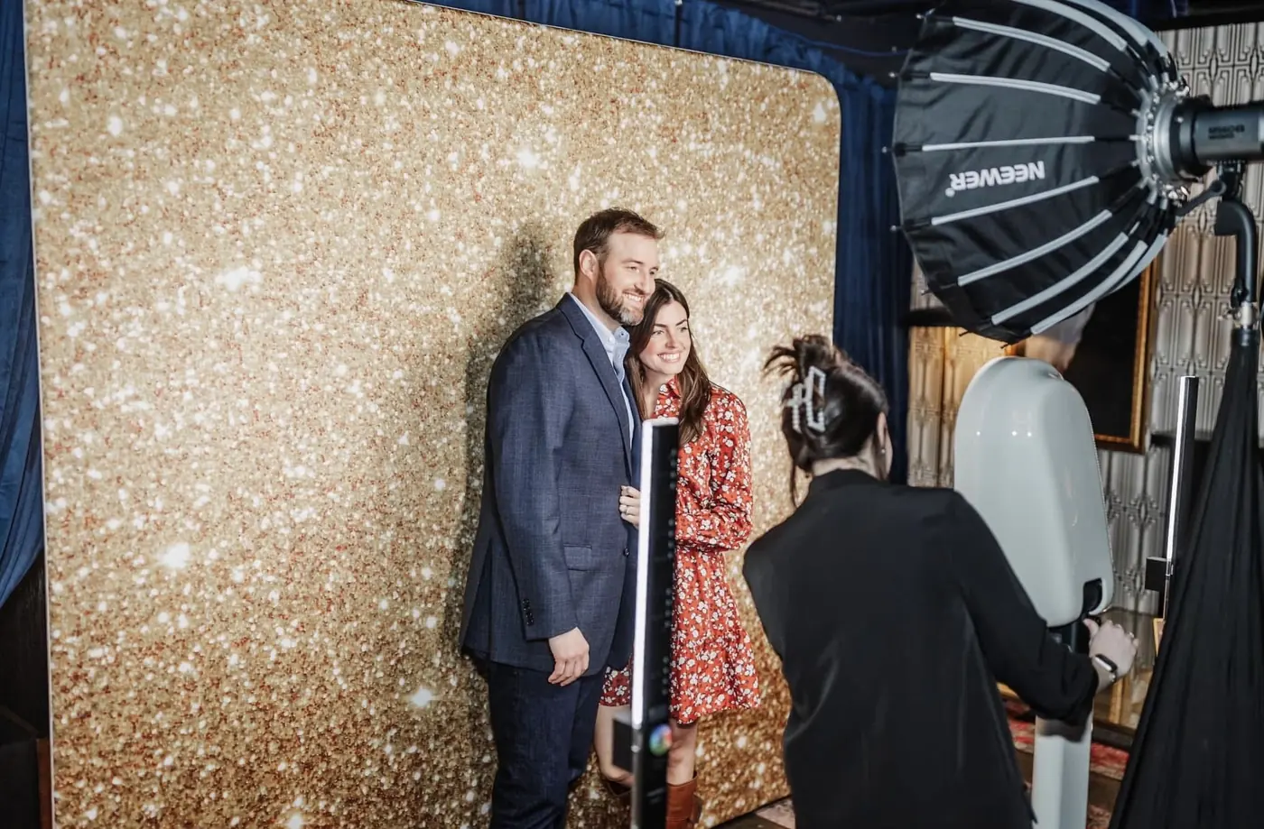 Two guests posing at the gold backdrop while the attendant works the booth beside them