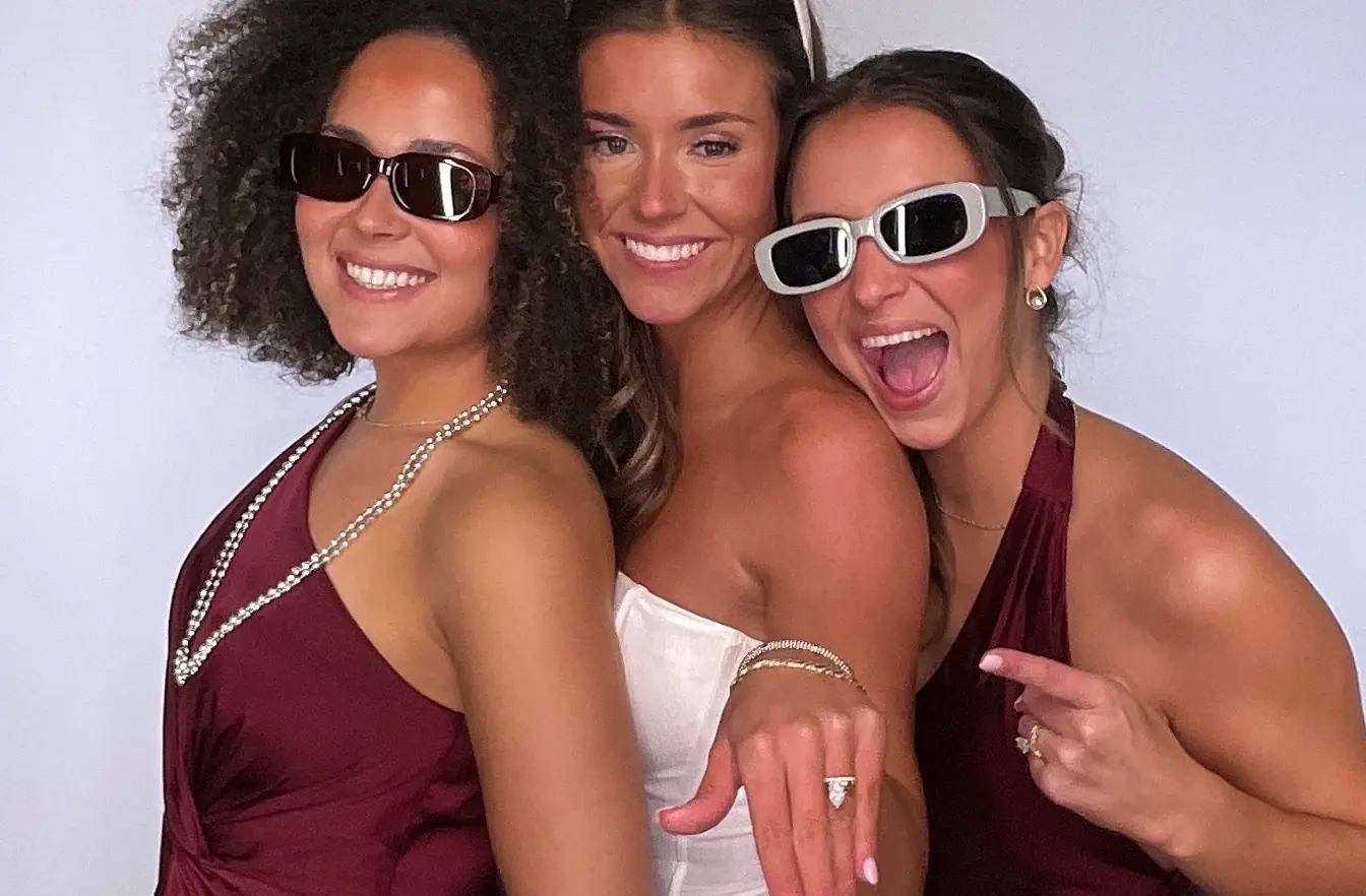 A bride laughing in the booth with two friends in sunglasses