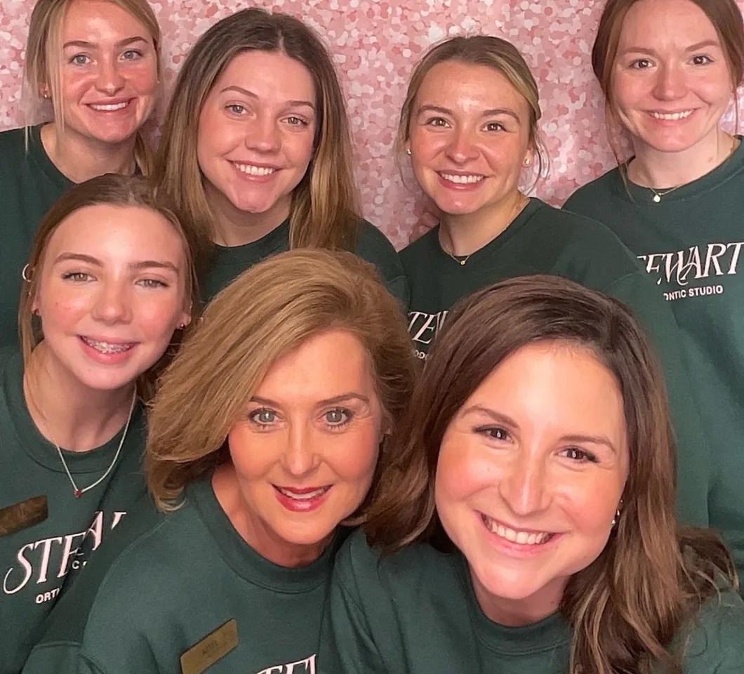 A group of guests in matching shirts crowded together in front of a pink sequin backdrop