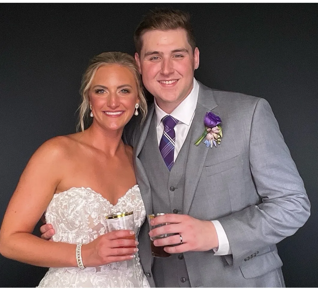 A bride and groom with drinks in hand, photographed in the booth against a charcoal backdrop